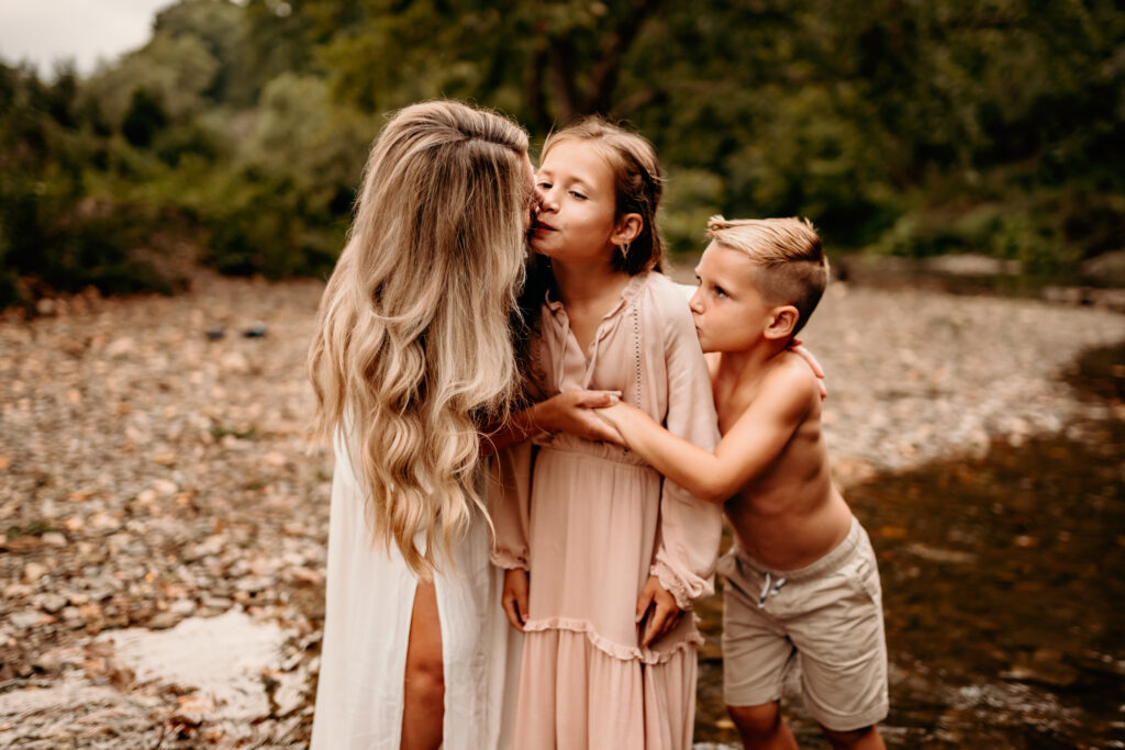 children kissing mom by creek