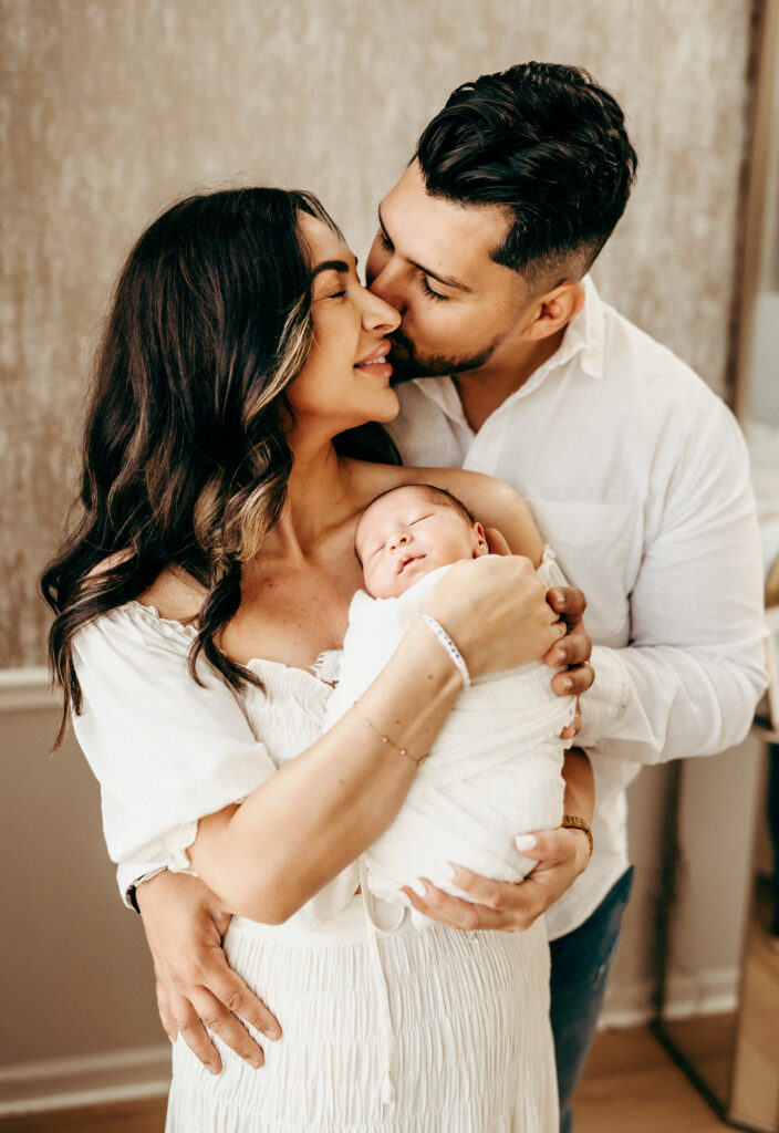 Family photos. Husband kissing wife holding baby
