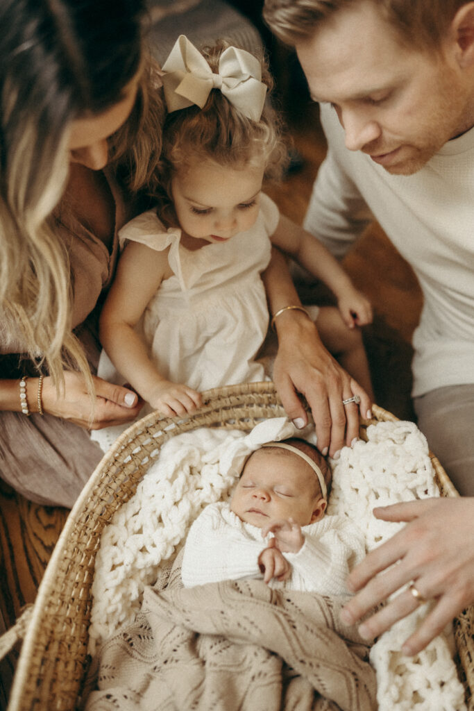 newborn family picture. family of 4 sitting next to baby in boho basket
