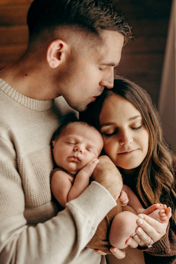 mom dad and baby cuddling close during newborn package
