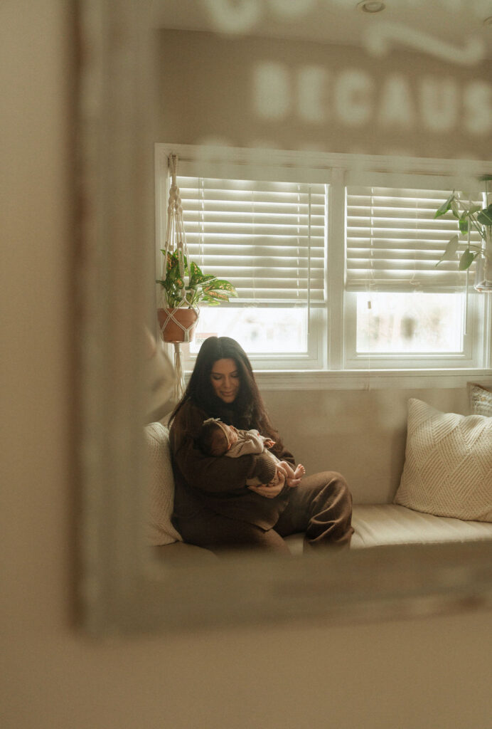 mom sitting in window nook with newborn baby girl, mirror photo