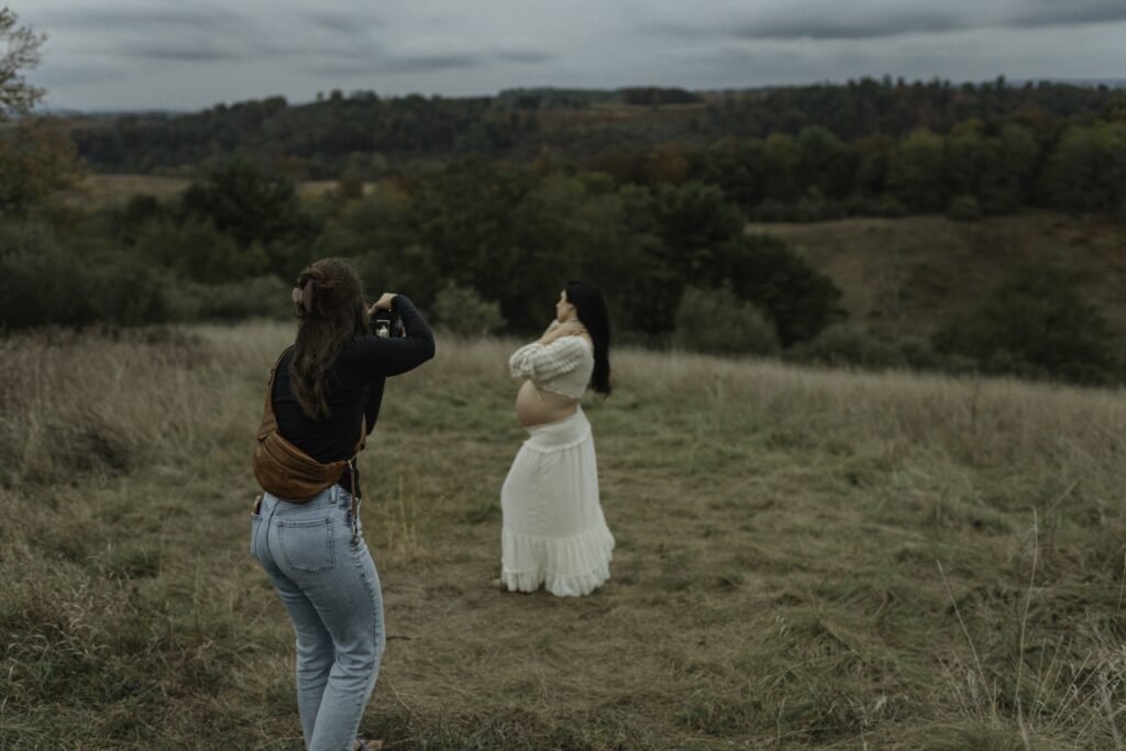 A photographer captures a stunning moment of a pregnant woman posing outdoors in a grassy field, surrounded by trees and hills—perfect for Lehigh Valley family photography.